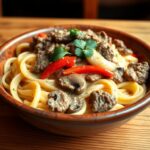 A plate of Philly cheesesteak pasta with tender fettuccine, creamy cheese sauce, seasoned steak strips, sautéed bell peppers, onions, and mushrooms, garnished with fresh parsley, served in a rustic bowl on a wooden table.